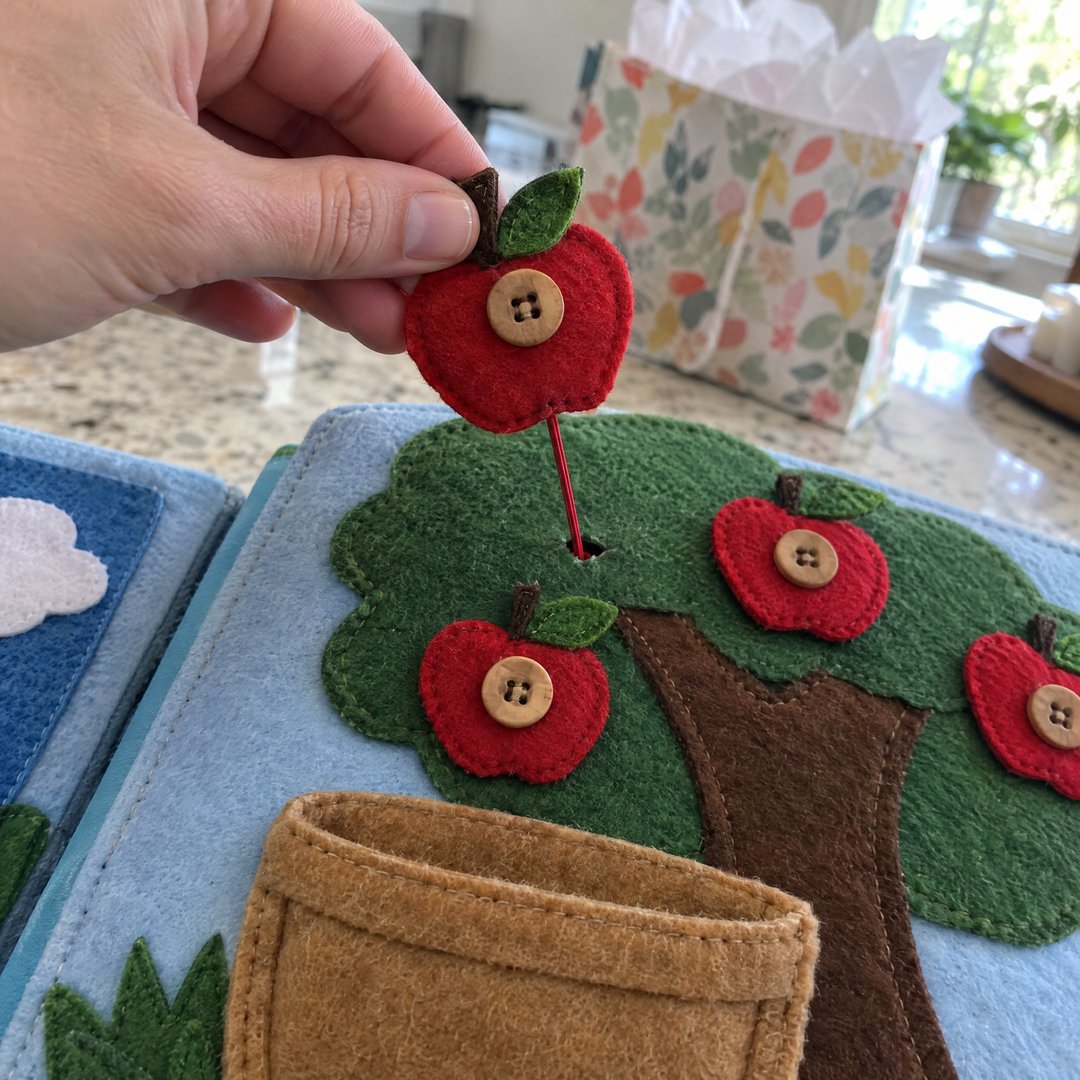 A hand tugging a stitched felt apple button to test it